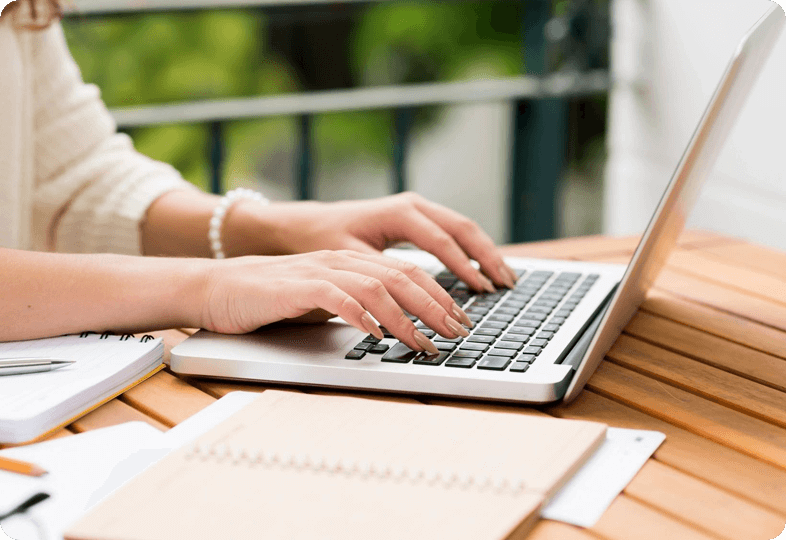 A woman typing on a laptop on a wooden table.